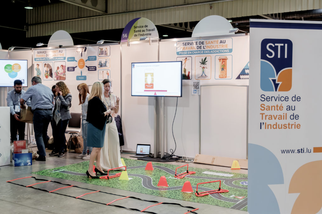 Des personnes sont sur un stand exposant devant un écran - Forum SST 2024